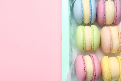 Photo of Many delicious colorful macarons in box on pink background, top view. Space for text