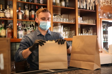 Photo of Waiter packing takeout orders in restaurant. Food service during coronavirus quarantine