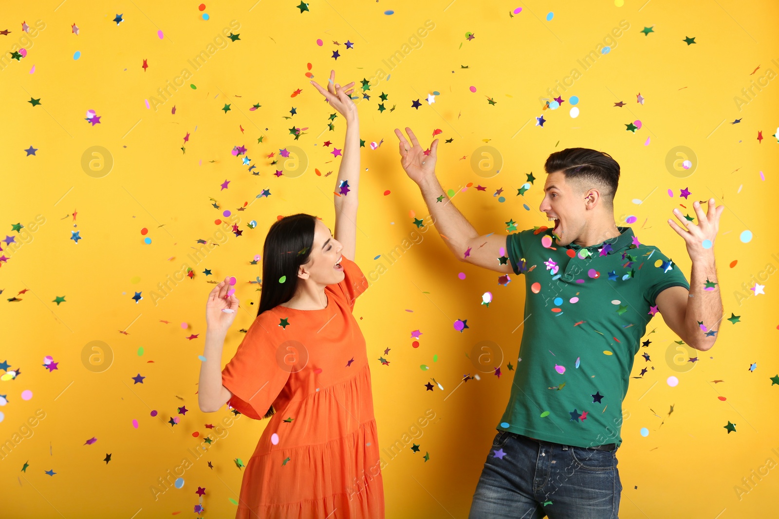 Photo of Happy couple and falling confetti on yellow background