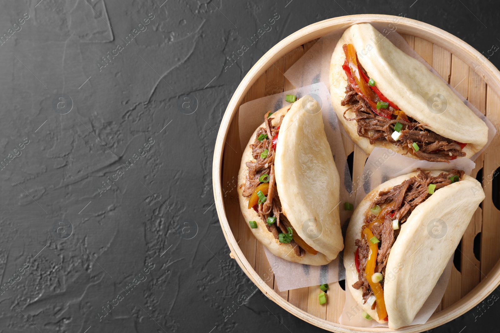 Photo of Delicious gua bao in bamboo steamer on black table, top view. Space for text