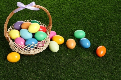Photo of Wicker basket with bow and bright painted Easter eggs on green grass