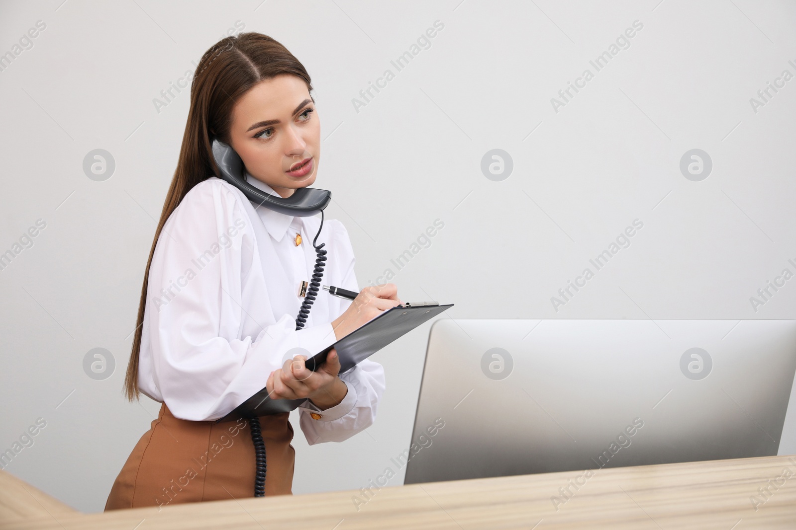 Photo of Female receptionist with clipboard talking on phone at workplace