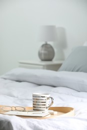 Photo of Mug of hot drink with stylish cup coaster, glasses and notebook on bed in room