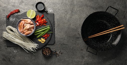 Photo of Flat lay composition with black wok, spices and products on dark textured table