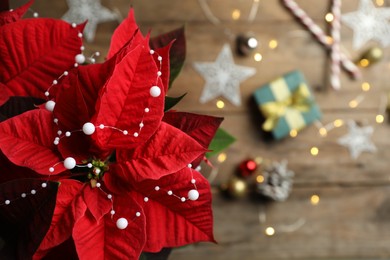 Photo of Poinsettia (traditional Christmas flower) with elegant bead garland and holiday items on wooden table, top view. Space for text