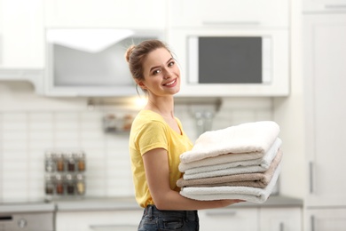 Photo of Woman holding folded clean towels in kitchen. Laundry day