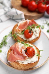Photo of Tasty rusks with prosciutto, cream cheese and tomatoes served on white table, closeup