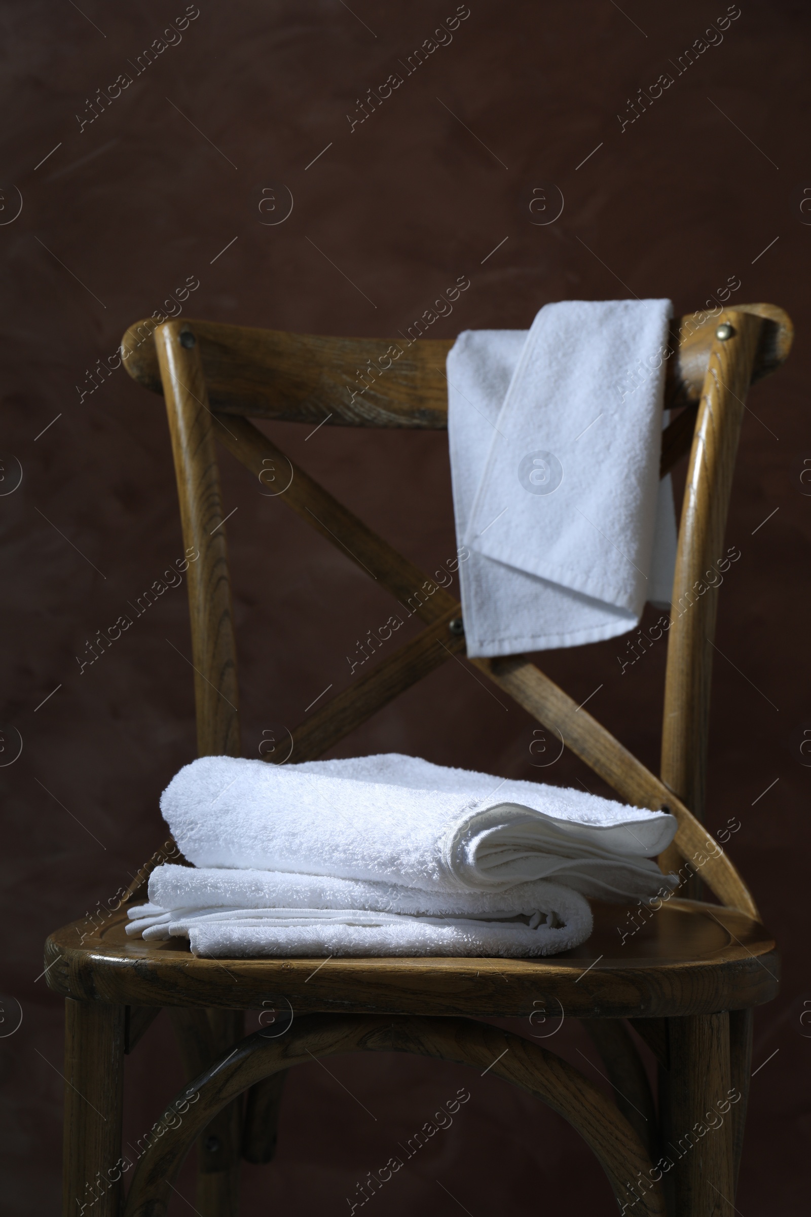 Photo of White terry towels on wooden chair against brown background