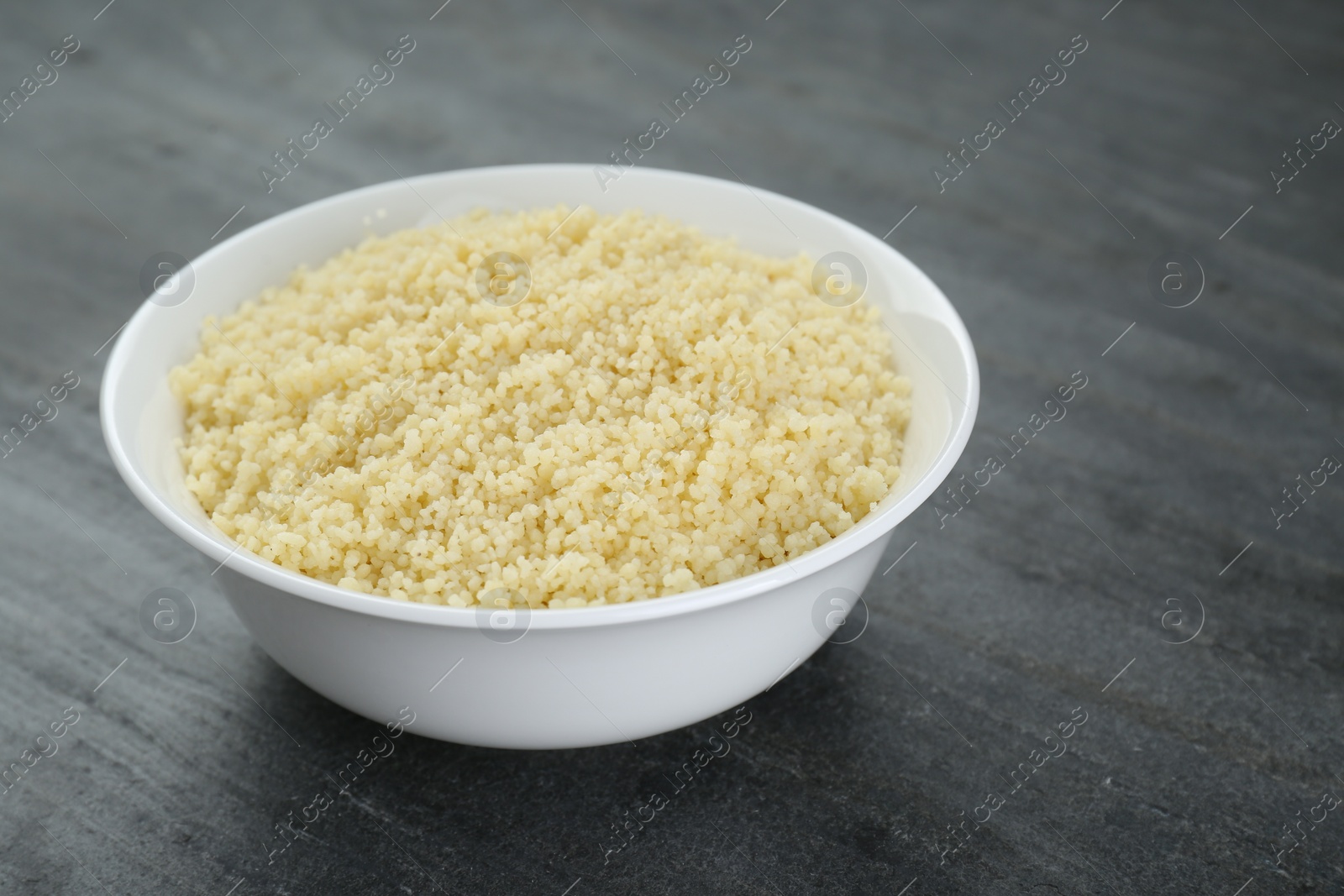 Photo of Bowl of tasty couscous on grey table, closeup