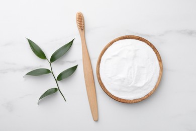 Bamboo toothbrush, green leaf and bowl of baking soda on white marble table, flat lay