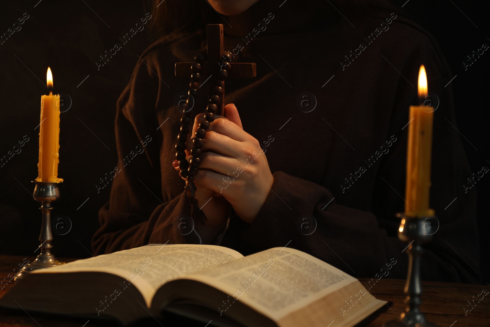 Photo of Woman praying at table with burning candles and Bible, closeup