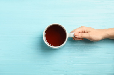 Photo of Woman with cup of tea at light blue wooden table, top view