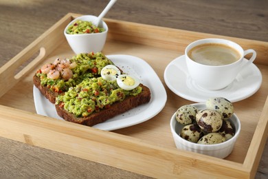 Slices of bread with tasty guacamole, eggs, shrimp and coffee on wooden table