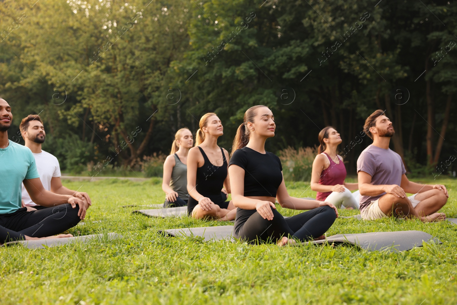 Photo of Group of people practicing yoga on mats outdoors. Lotus pose