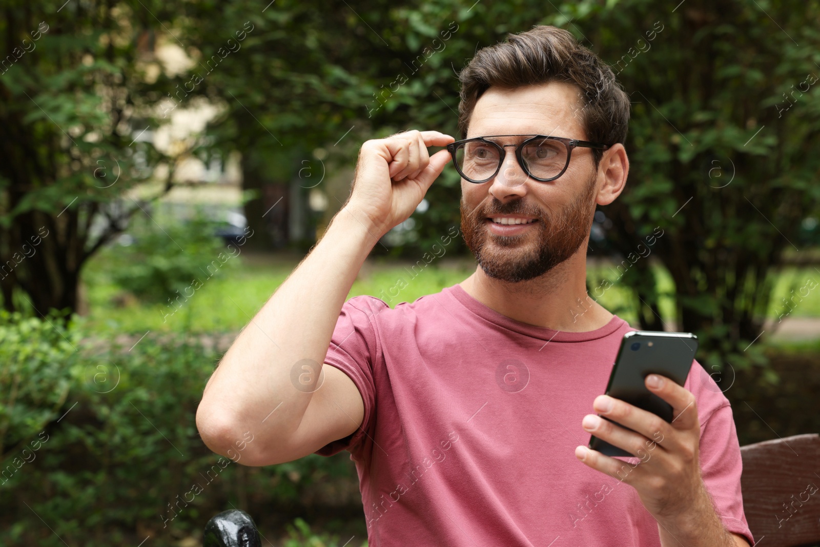 Photo of Handsome man using smartphone in park, space for text