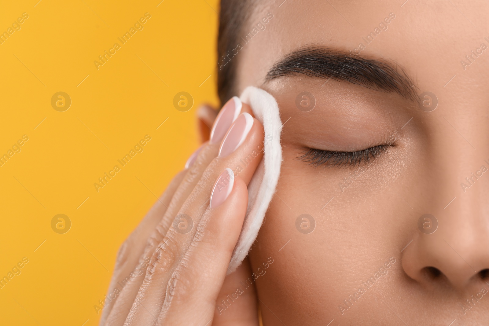 Photo of Beautiful woman removing makeup with cotton pad on orange background, closeup. Space for text