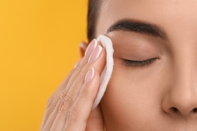 Beautiful woman removing makeup with cotton pad on orange background, closeup. Space for text