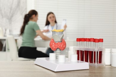 Photo of Endocrinologist examining patient at clinic, focus on model of thyroid gland and blood samples in test tubes