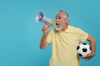Emotional senior sports fan with soccer ball using megaphone on light blue background, space for text