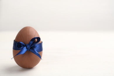 Sweet chocolate egg with blue bow on white wooden table. Space for text