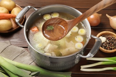 Photo of Pot with tasty bouillon and different ingredients on wooden table