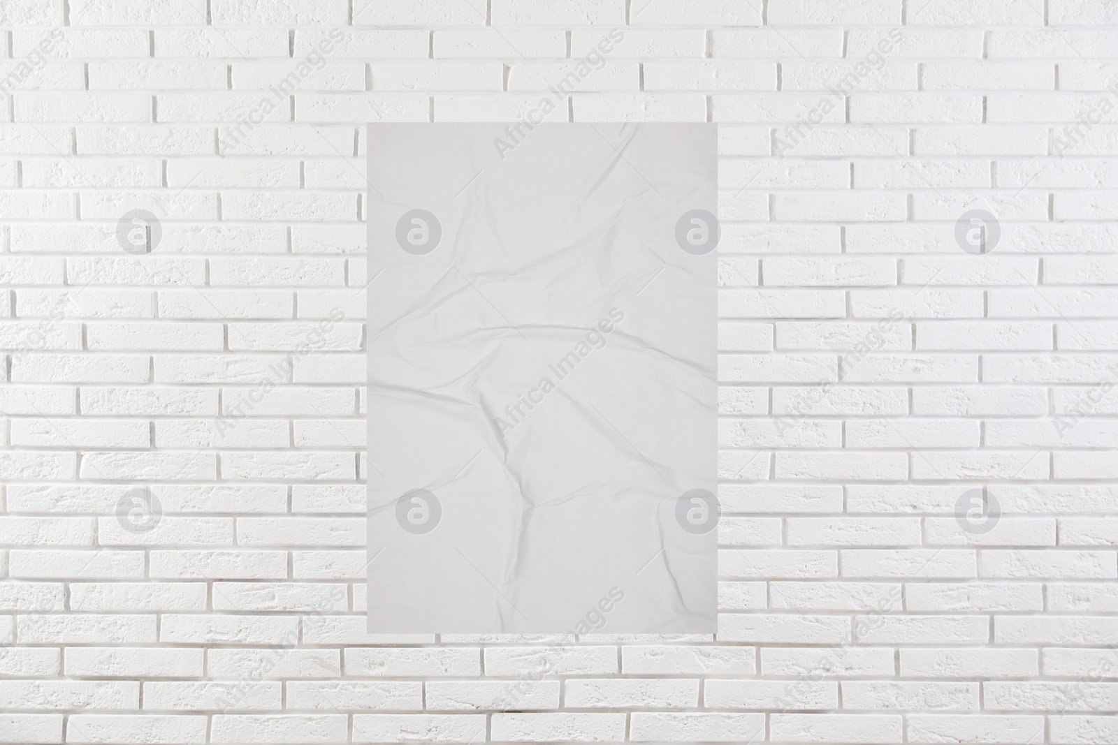 Image of Blank creased poster on white brick wall. Mockup for design 