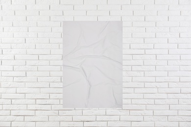 Image of Blank creased poster on white brick wall. Mockup for design 