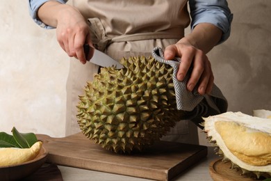 Photo of Woman cutting fresh ripe durian at table, closeup