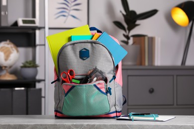 Photo of Children's backpack with different school stationery on table indoors