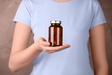 Woman holding bottle with vitamin capsules against light brown background, closeup