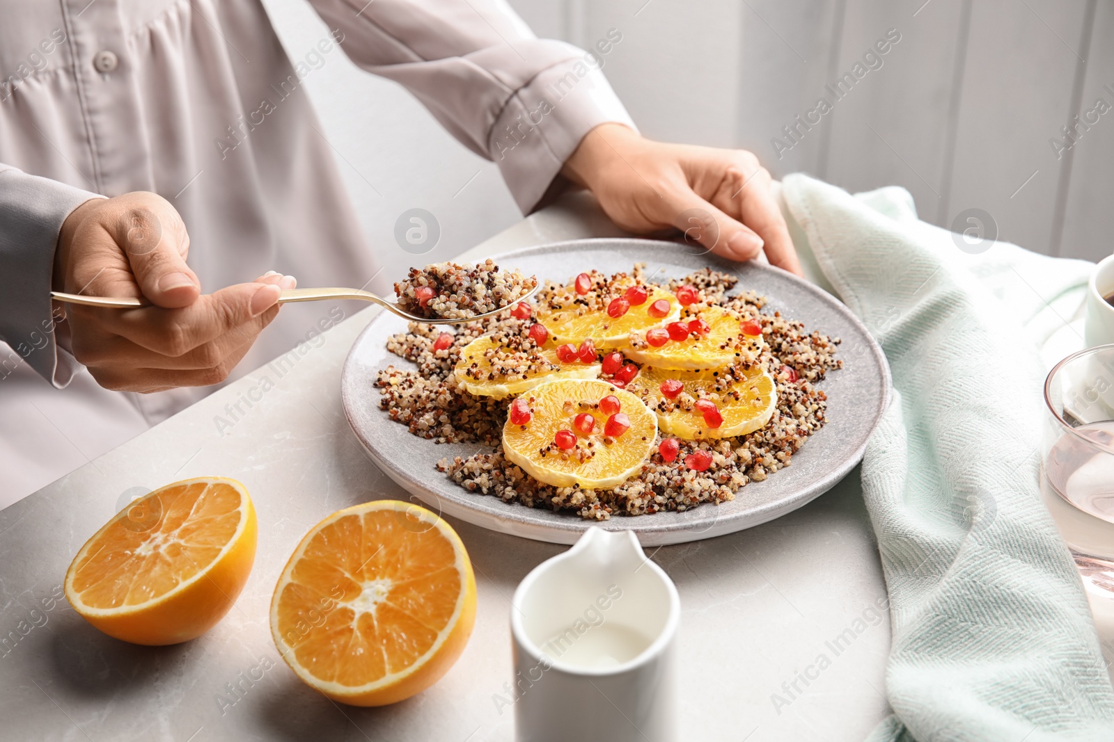 Photo of Woman eating quinoa porridge with orange and pomegranate seeds at table, closeup