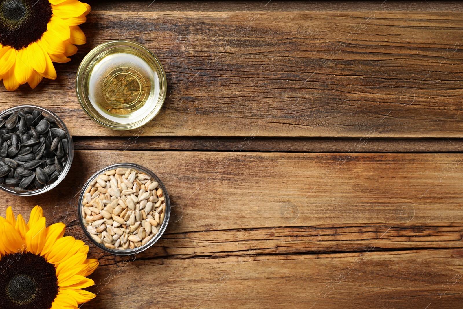 Photo of Bowls with sunflower cooking oil and seeds near flowers on wooden table, flat lay. Space for text