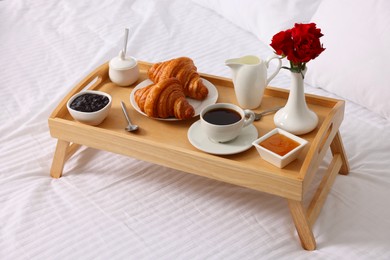 Photo of Tasty breakfast served in bed. Fresh croissants, coffee, jam and honey on wooden tray
