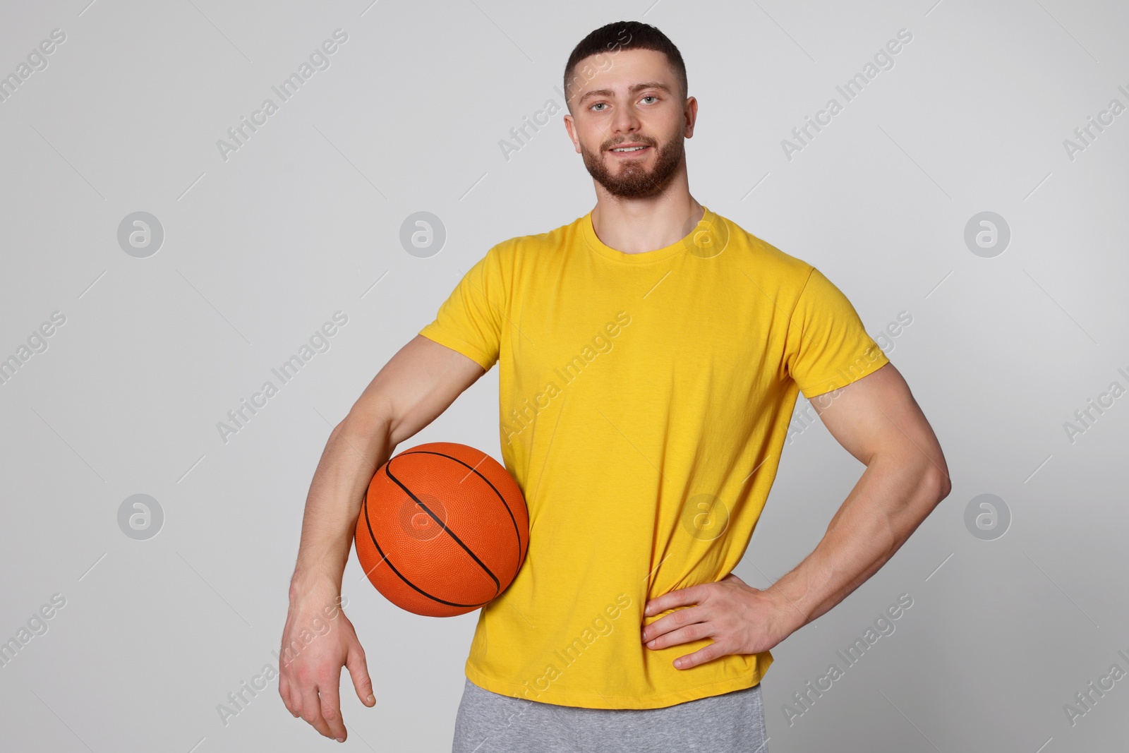 Photo of Athletic young man with basketball ball on light grey background