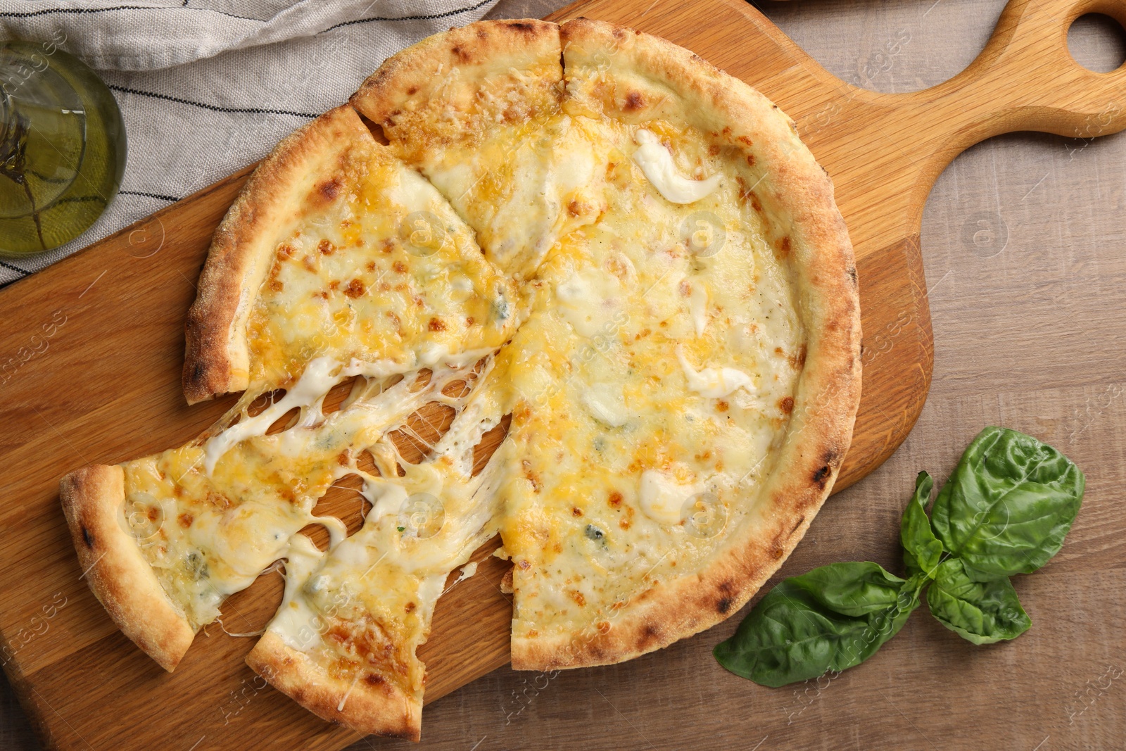 Photo of Delicious cut cheese pizza, basil and oil on wooden table, flat lay