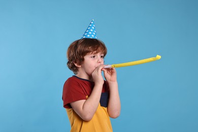 Photo of Birthday celebration. Cute little boy in party hat with blower on light blue background