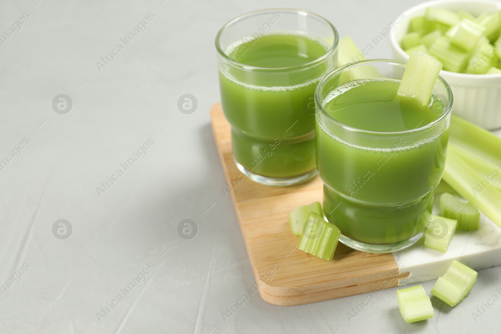 Photo of Celery juice and fresh vegetables on light gray table, closeup. Space for text