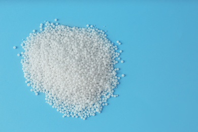 Photo of Pellets of ammonium nitrate on light blue background, flat lay with space for text. Mineral fertilizer