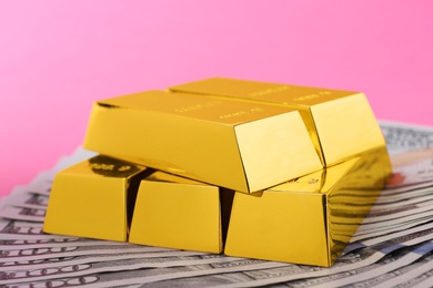 Shiny gold bars and dollar bills on color background