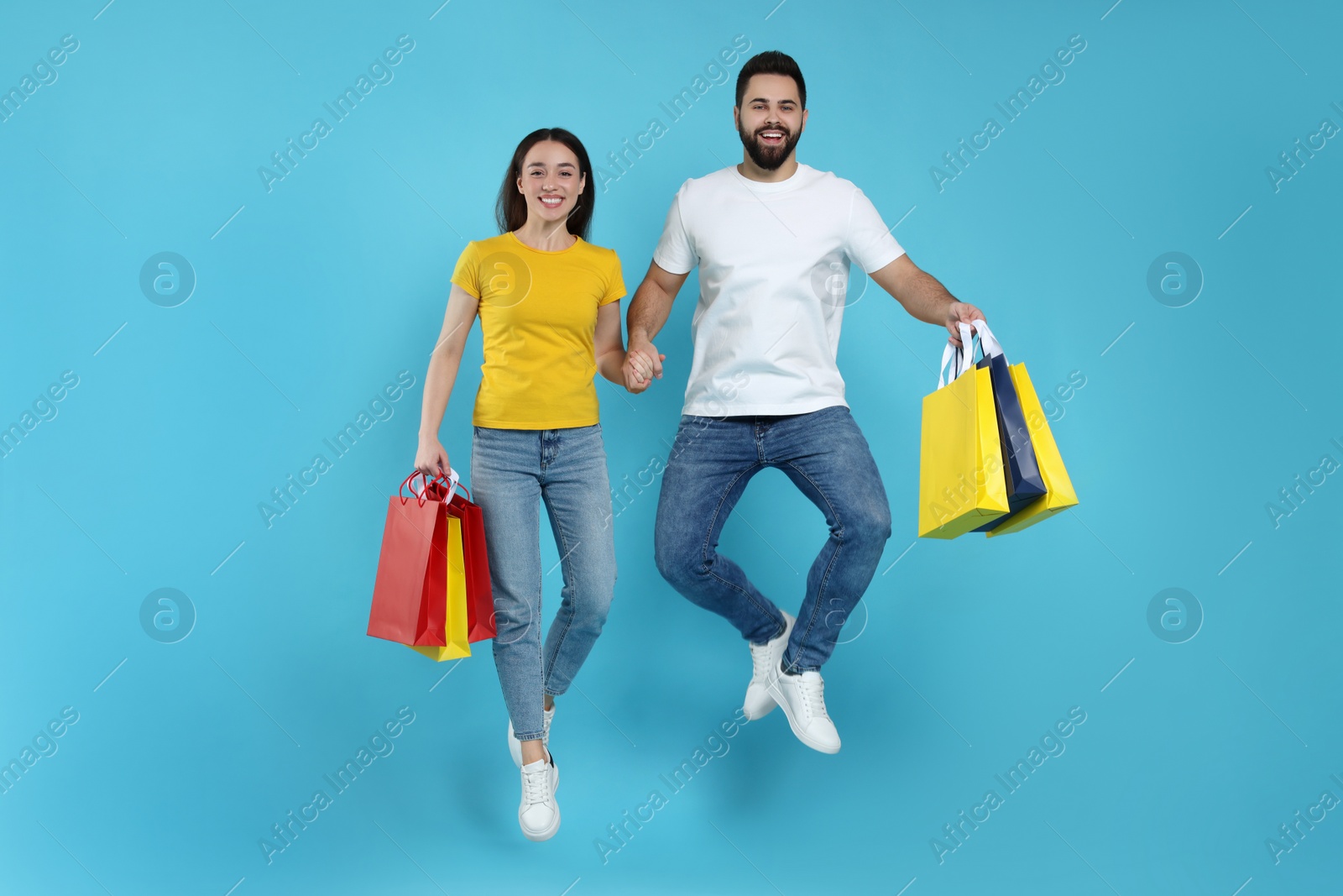 Photo of Happy couple with shopping bags jumping on light blue background