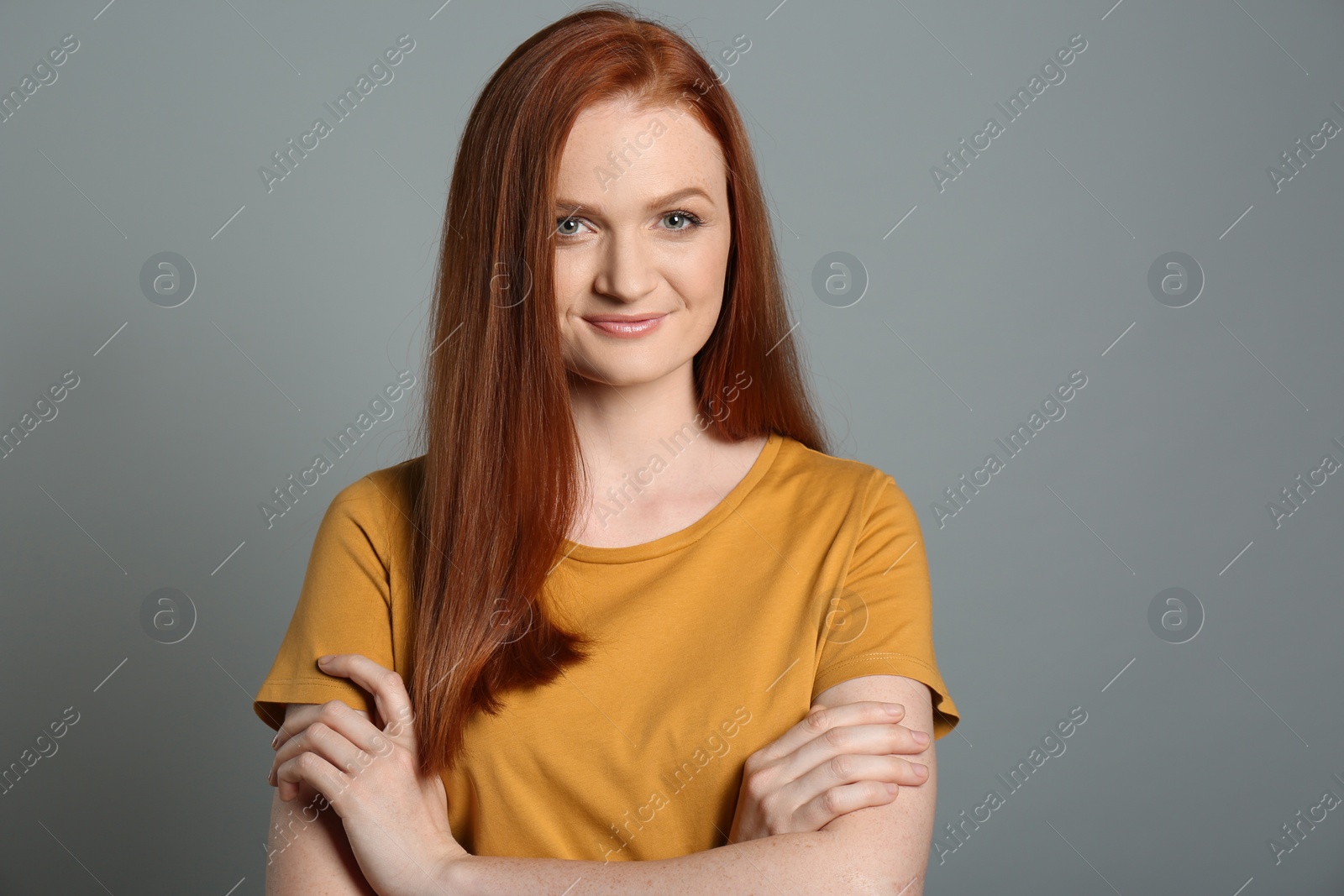 Photo of Candid portrait of happy young woman with charming smile and gorgeous red hair on grey background