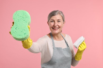 Photo of Happy housewife with sponge and brush on pink background