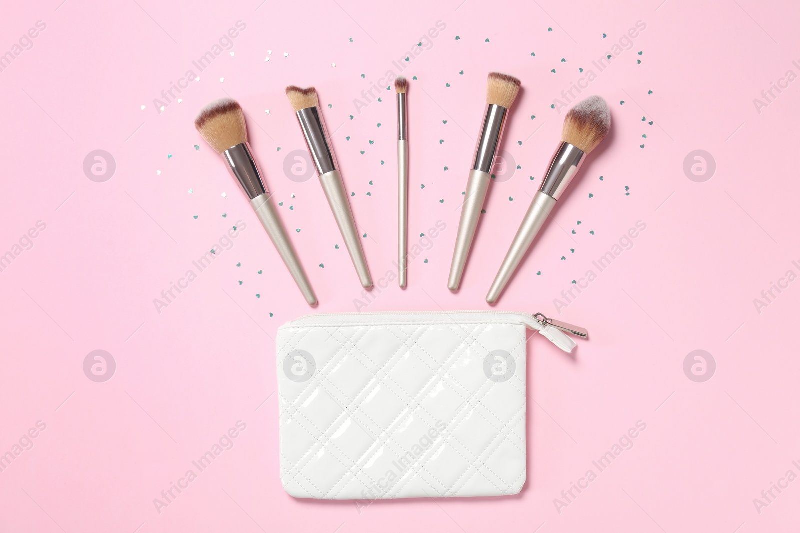 Photo of Bag and different makeup brushes on pink background, flat lay