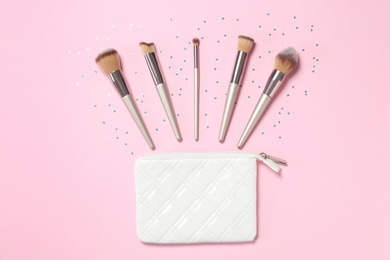 Photo of Bag and different makeup brushes on pink background, flat lay