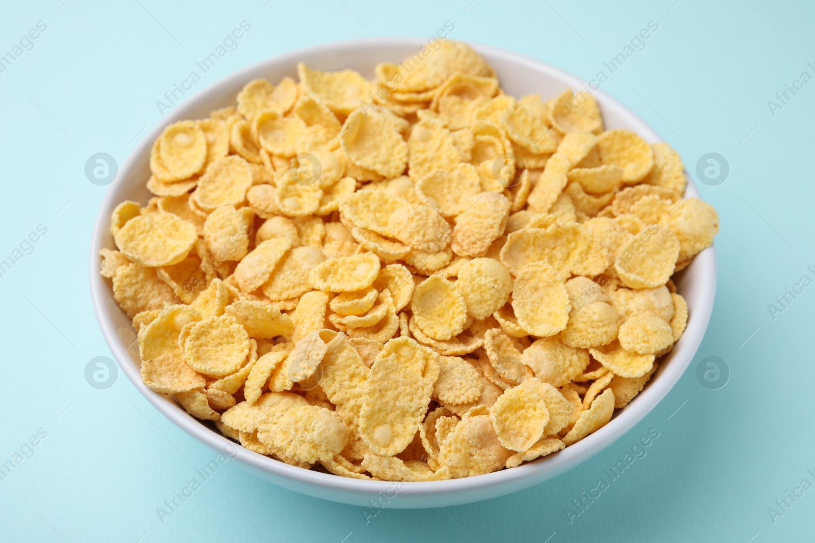 Photo of Breakfast cereal. Tasty corn flakes in bowl on light blue table, closeup