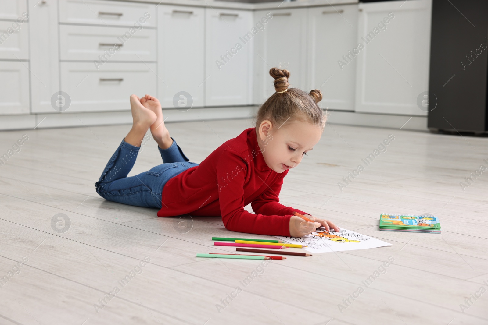 Photo of Cute little girl coloring on warm floor in kitchen. Heating system