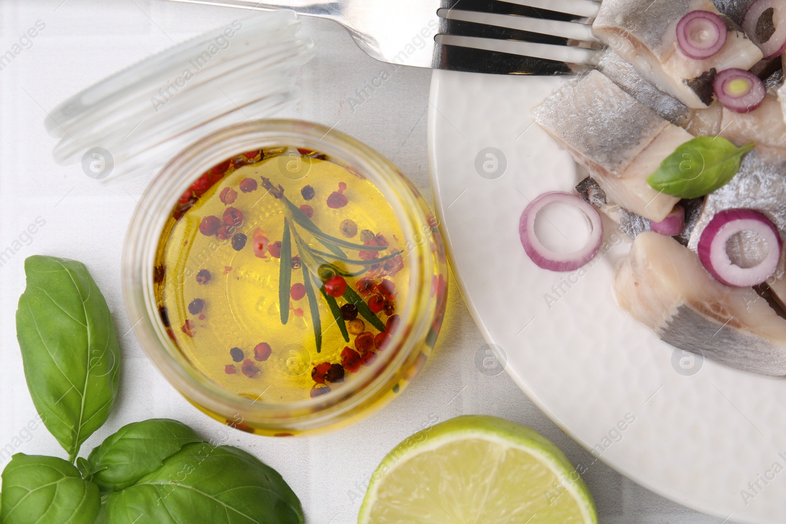 Photo of Tasty fish marinade in jar and herring on light tiled table, flat lay