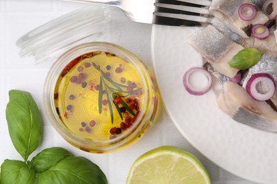 Photo of Tasty fish marinade in jar and herring on light tiled table, flat lay