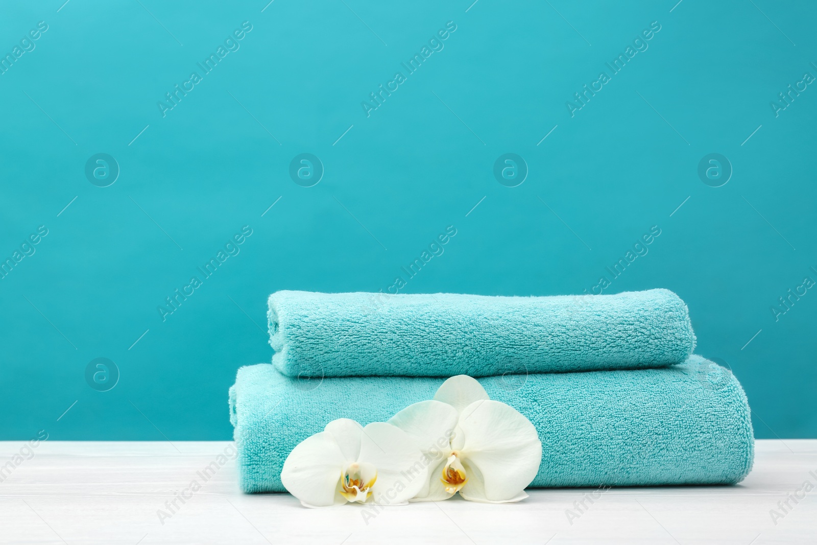 Photo of Stack of soft clean towels with beautiful flowers on table against color background. Space for text