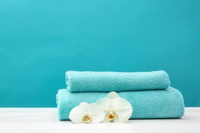 Stack of soft clean towels with beautiful flowers on table against color background. Space for text